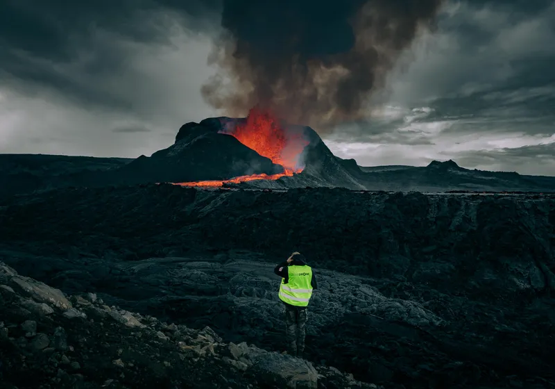 A person in a yellow vest in front of the active volcano on the Reykjanes peninsula